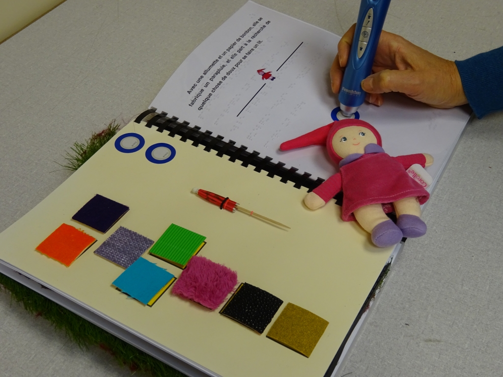 Photo du livre tactile "la très petite poupée" avec le stylo lecteur de puce RFID permettant d'avoir accès aux enregistrements sonores